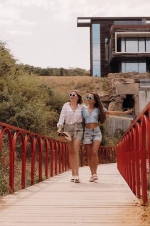 Téléchargez les photos : Deux jeunes femmes joyeuses embrassant et souriant tout en marchant ensemble à l'extérieur - en image libre de droit