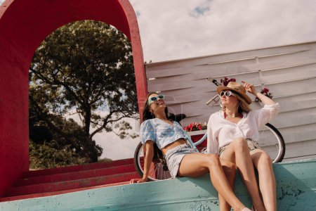 Téléchargez les photos : Deux jeunes femmes heureuses regardant détendues tout en appréciant la journée d'été en plein air ensemble - en image libre de droit