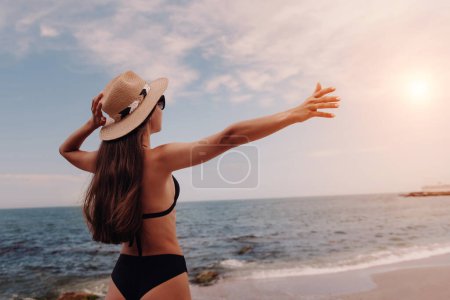 Photo for Rear view of young woman in swimwear adjusting hat while enjoying sea view on the beach - Royalty Free Image