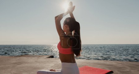 Photo for Rear view of young woman in sportswear practicing yoga while sitting in lotus position seaside - Royalty Free Image
