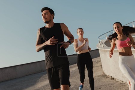 Téléchargez les photos : Trois jeunes concentrés en vêtements de sport profitant du jogging matinal en plein air ensemble - en image libre de droit