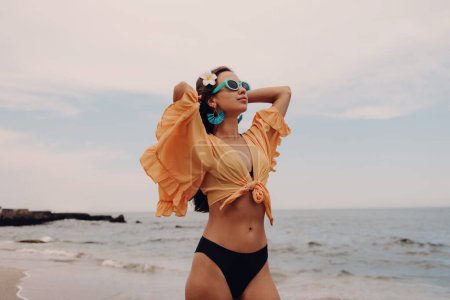 Téléchargez les photos : Jeune femme à la mode étirant les mains tout en profitant de la journée sur la plage - en image libre de droit
