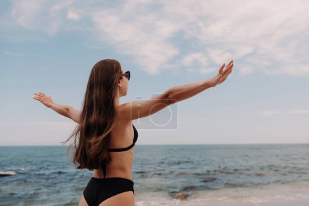 Téléchargez les photos : Vue arrière de la belle femme étirant les mains tout en profitant de la vue sur la mer sur la plage - en image libre de droit