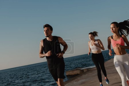 Téléchargez les photos : Groupe de jeunes en tenue de sport concentrés tout en faisant du jogging au bord de la mer ensemble - en image libre de droit
