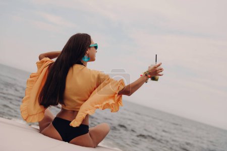 Photo for Rear view of fashionable young woman in boho styled crop top enjoying cocktail seaside - Royalty Free Image