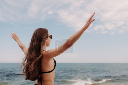 Téléchargez les photos : Vue arrière de la jeune femme étirant les mains tout en profitant de la vue sur la mer sur la plage - en image libre de droit