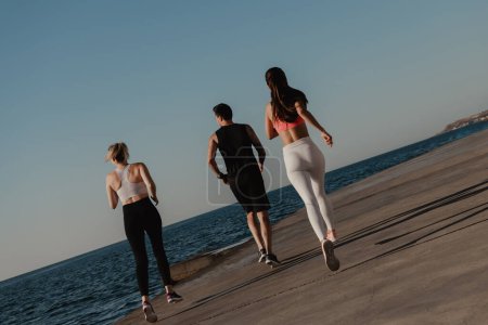Téléchargez les photos : Vue arrière de jeunes en vêtements de sport profitant du jogging matinal au bord de la mer ensemble - en image libre de droit