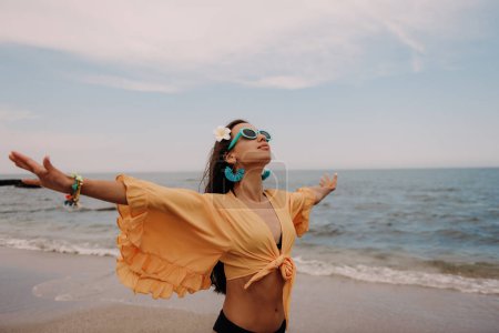 Téléchargez les photos : Jeune femme à la mode étirant les mains tout en profitant de la journée sur la plage - en image libre de droit