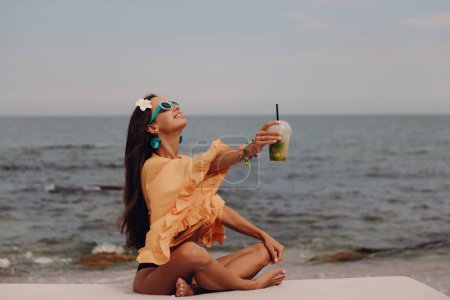 Photo for Attractive young woman in boho styled crop top enjoying cocktail while relaxing seaside - Royalty Free Image