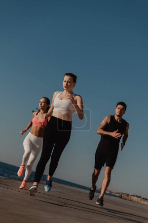 Téléchargez les photos : Trois jeunes gens confiants en vêtements de sport à l'air concentré tout en courant au bord de la mer ensemble - en image libre de droit