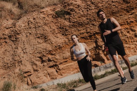 Téléchargez les photos : Jeune couple confiant en vêtements de sport courir contre la montagne tout en s'entraînant à l'extérieur ensemble - en image libre de droit