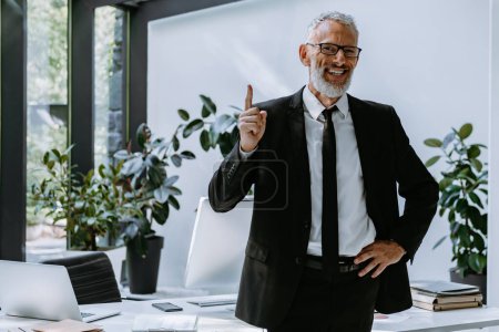 Photo for Happy mature businessman pointing up while standing in the modern office - Royalty Free Image