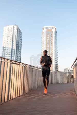 Téléchargez les photos : Pleine longueur de jeune athlète africain confiant en vêtements de sport profitant du jogging matinal en plein air - en image libre de droit