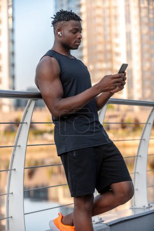 Foto de Hombre africano joven en ropa deportiva comprobar su programa de fitness mientras se utiliza el teléfono inteligente al aire libre - Imagen libre de derechos