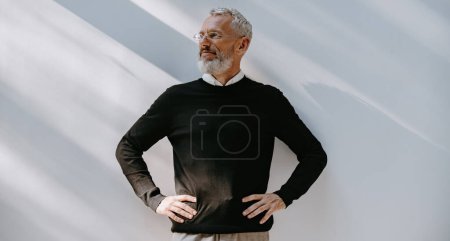 Photo for Portrait of confident mature man in smart casual wear holding hands on hip while standing against a wall - Royalty Free Image