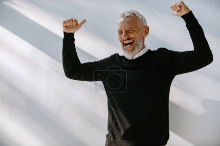Téléchargez les photos : Joyeux homme âgé en tenue décontractée intelligente regardant excité tout en faisant un geste contre le mur - en image libre de droit