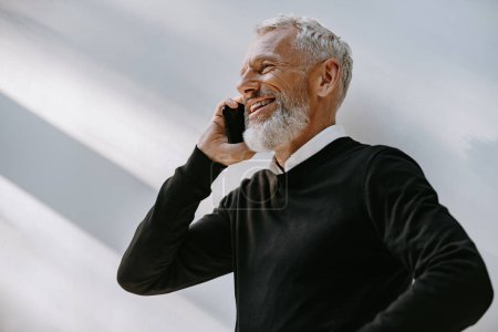 Foto de Retrato de hombre mayor feliz hablando en el teléfono móvil y sonriendo mientras está de pie contra la pared - Imagen libre de derechos