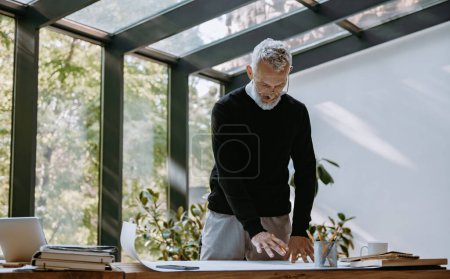 Photo for Confident mature architect examining blueprint while working in the creative office - Royalty Free Image