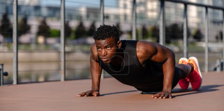 Téléchargez les photos : Un jeune Africain confiant en vêtements de sport faisant des pompes tout en faisant de l'exercice à l'extérieur - en image libre de droit