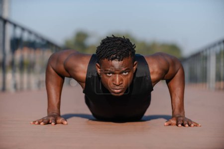 Téléchargez les photos : Jeune athlète africain concentré en tenue de sport faisant des pompes pendant l'exercice à l'extérieur - en image libre de droit