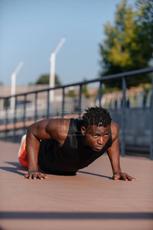 Téléchargez les photos : Athlète africain fort en tenue de sport faisant des pompes tout en faisant de l'exercice à l'extérieur - en image libre de droit