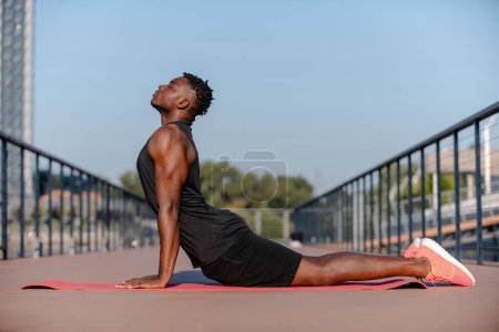 Photo for Confident young African man in sportswear doing stretching exercises outdoors - Royalty Free Image