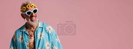 Photo for Cool senior man in stylish shirt and floral wreath on head smiling against pink background - Royalty Free Image