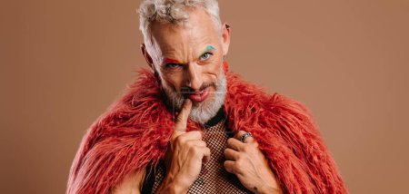 Téléchargez les photos : Mature gay homme avec arc-en-ciel coloré sourcils portant manteau moelleux sur fond brun - en image libre de droit