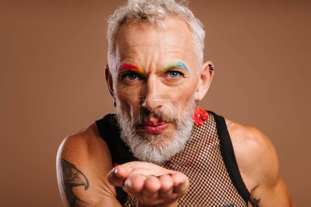 Téléchargez les photos : Barbu mature gay l'homme avec scène maquillage soufflant un baiser sur brun fond - en image libre de droit
