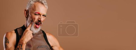 Téléchargez les photos : Ludique mature gay l'homme avec arc-en-ciel coloré sourcils toucher visage avec doigt sur brun fond - en image libre de droit