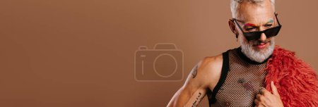 Téléchargez les photos : Homme gay mature à la mode avec des sourcils colorés portant manteau moelleux sur fond brun - en image libre de droit