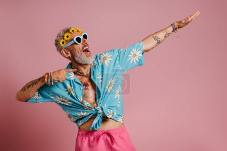Foto de El hombre mayor a la moda en la corona floral que apunta lejos y sonríe sobre el fondo rosa - Imagen libre de derechos