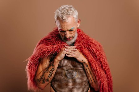 Foto de Retrato de hombre gay maduro con cejas de color arco iris con abrigo esponjoso contra fondo marrón - Imagen libre de derechos