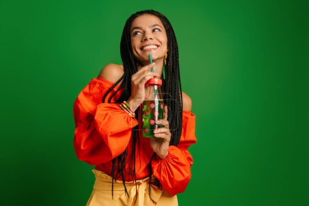 Photo for Attractive young woman enjoying fresh lemonade and smiling against green background - Royalty Free Image