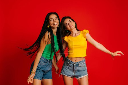 Photo for Two happy young women in colorful wear dancing against red background - Royalty Free Image