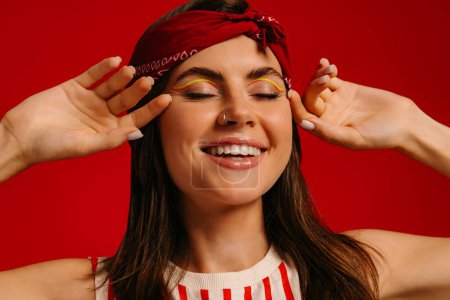 Téléchargez les photos : Gros plan portrait d'une jeune femme hipster heureuse gardant les yeux fermés sur fond rouge - en image libre de droit