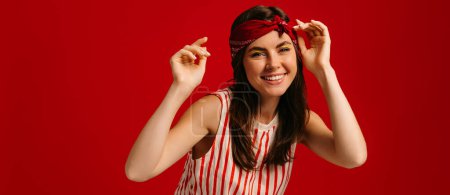 Téléchargez les photos : Joyeux jeune hipster femme dansant et souriant tout en se tenant debout sur fond rouge - en image libre de droit