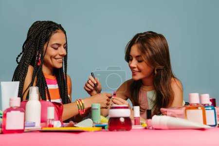 Photo for Two happy female presenters testing various beauty products while sitting at the desk on blue background - Royalty Free Image