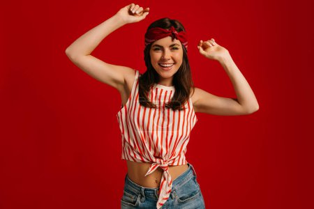 Téléchargez les photos : Jeune femme hipster élégante dansant et souriant debout sur fond rouge - en image libre de droit