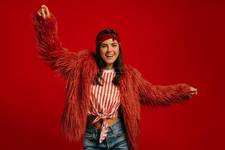 Foto de Mujer hipster joven de moda con abrigo esponjoso y bailando sobre fondo rojo - Imagen libre de derechos