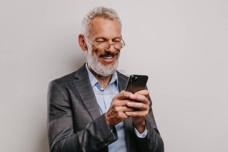 Foto de Retrato de hombre de negocios maduro feliz en formalwear mensajes de texto en el teléfono inteligente contra fondo blanco - Imagen libre de derechos