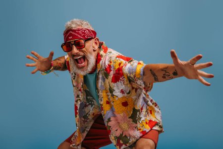 Téléchargez les photos : Cool hipster senior homme en chemise funky élégant geste et crier sur fond bleu - en image libre de droit