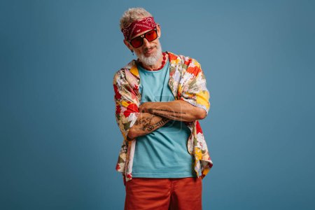 Téléchargez les photos : Cool hipster senior homme en chemise élégante funky garder les bras croisés sur fond bleu - en image libre de droit