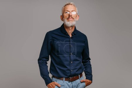 Téléchargez les photos : Homme mature confiant en tenue décontractée intelligente regardant la caméra sur fond gris - en image libre de droit