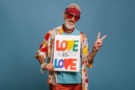 Téléchargez les photos : Joyeux hipster senior homme en chemise funky tenant bannière et geste sur fond bleu - en image libre de droit