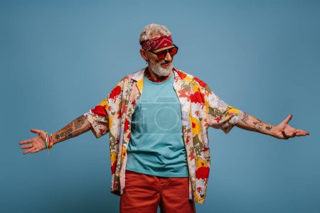 Téléchargez les photos : Cool hipster senior homme en chemise funky élégant geste et sourire sur fond bleu - en image libre de droit