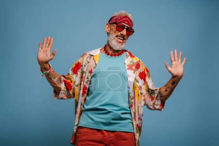 Foto de Hombre mayor hipster feliz en camisa funky elegante gesto sobre fondo azul - Imagen libre de derechos