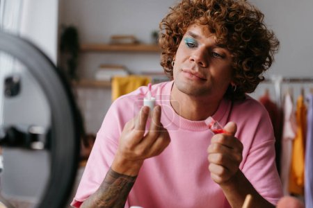 Foto de Confiado joven gay hombre examinar belleza productos mientras streaming maquillaje vlog desde casa - Imagen libre de derechos