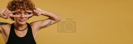 Photo for Playful young gay man showing his eye make-up and smiling against yellow background - Royalty Free Image