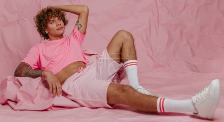 Foto de Moda joven gay hombre en moda desgaste apoyado en arrugado fajo de papel rosa contra fondo de color - Imagen libre de derechos